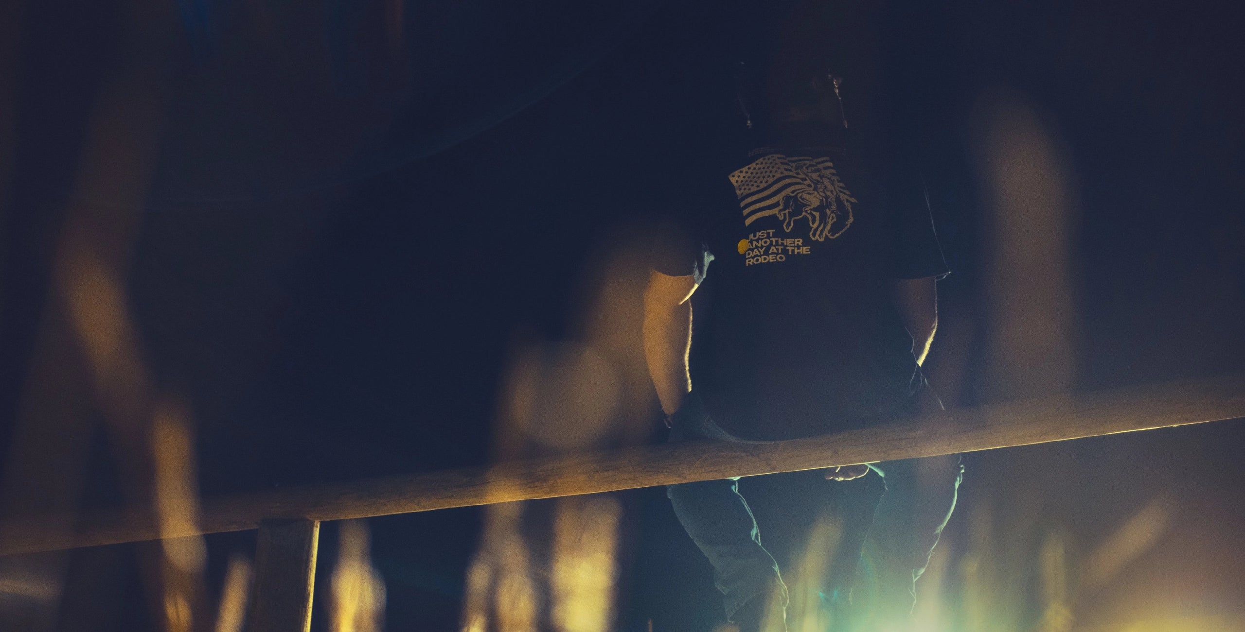 Imaginary Friends merch banner showing another day at the rodeo t shirt. man sitting on montana fence at night time.